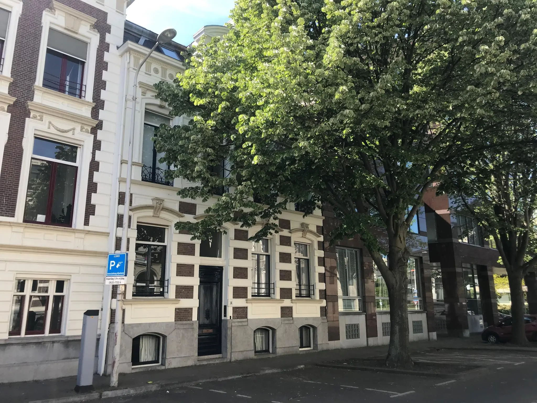 Voorgevels van statige herenhuizen aan de Burgemeester van Karnebeeklaan met bomen en parkeerplaatsen op de voorgrond.